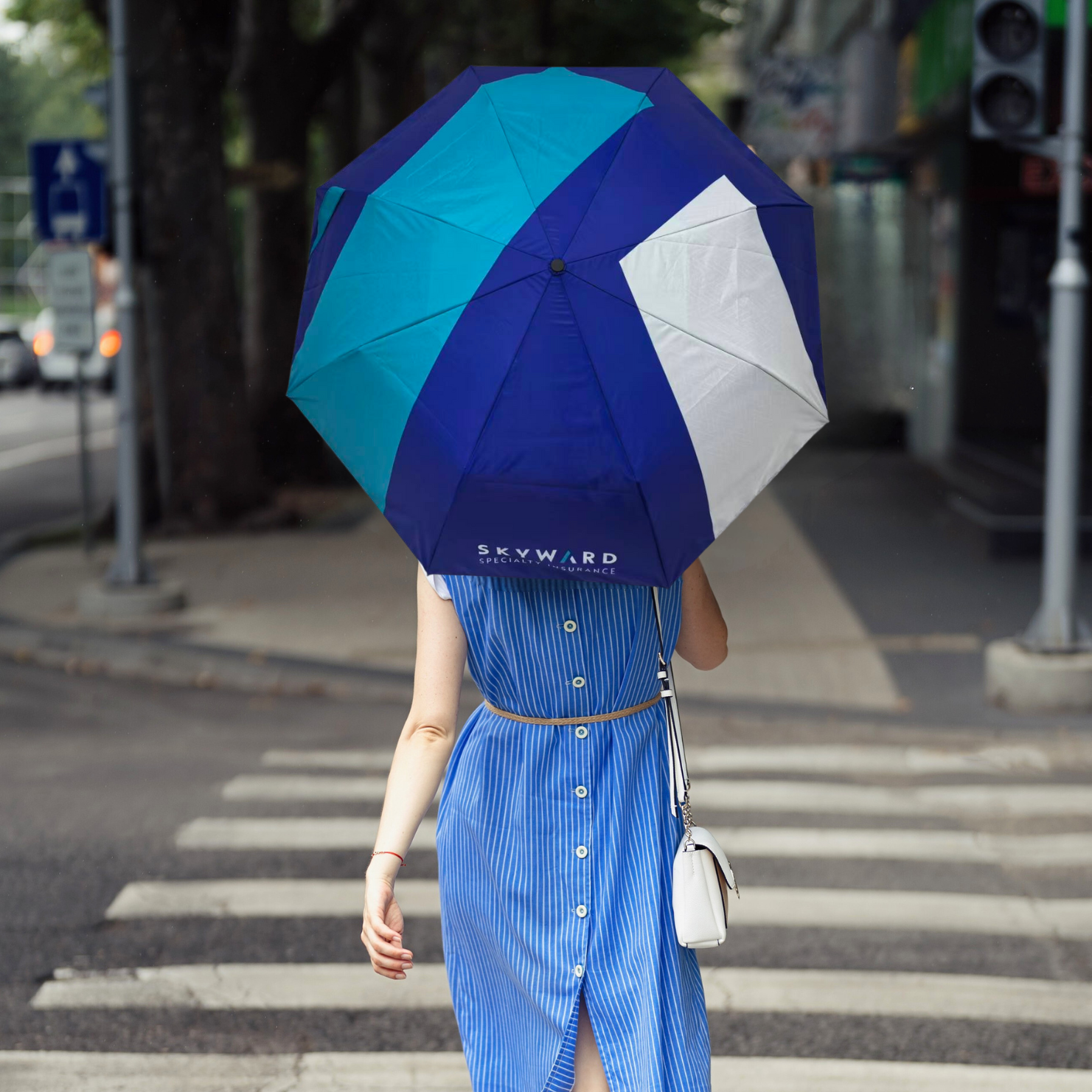 Person holding a blue and white umbrella on a city street
