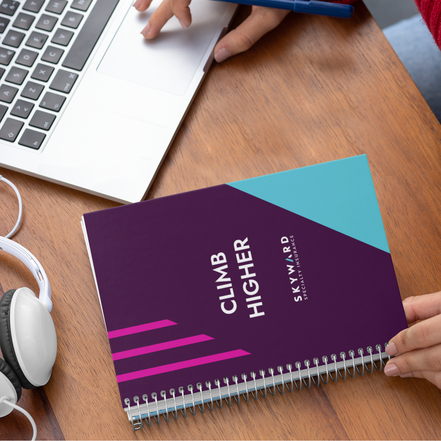 Person using a laptop with a 'Climb Higher' notebook on a desk